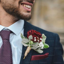Homem sorrindo usando terno azul-marinho com flor na lapela, representando elegância masculina em ocasiões especiais.