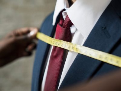 Fita métrica sendo usada para medir um terno masculino, destacando ajuste e precisão na confecção.