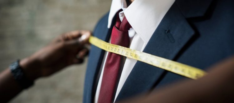 Fita métrica sendo usada para medir um terno masculino, destacando ajuste e precisão na confecção.