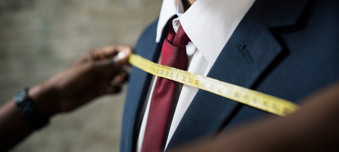 Fita métrica sendo usada para medir um terno masculino, destacando ajuste e precisão na confecção.