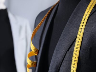 Blazer masculino em manequim com fita métrica sobre os ombros, representando alfaiataria e ajustes sob medida.