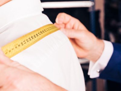 Alfaiate realizando medição dos ombros de um cliente para confecção de roupa sob medida.