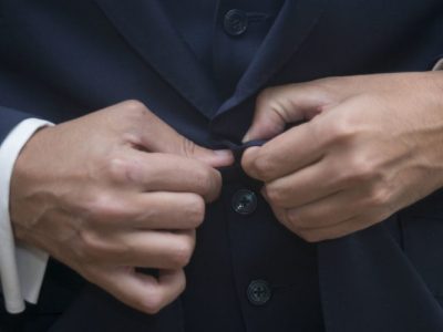 Homem ajustando o botão de um terno azul-marinho, destacando o caimento e o acabamento da alfaiataria.