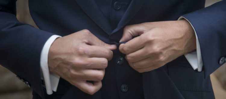 Homem ajustando o botão de um terno azul-marinho, destacando o caimento e o acabamento da alfaiataria.